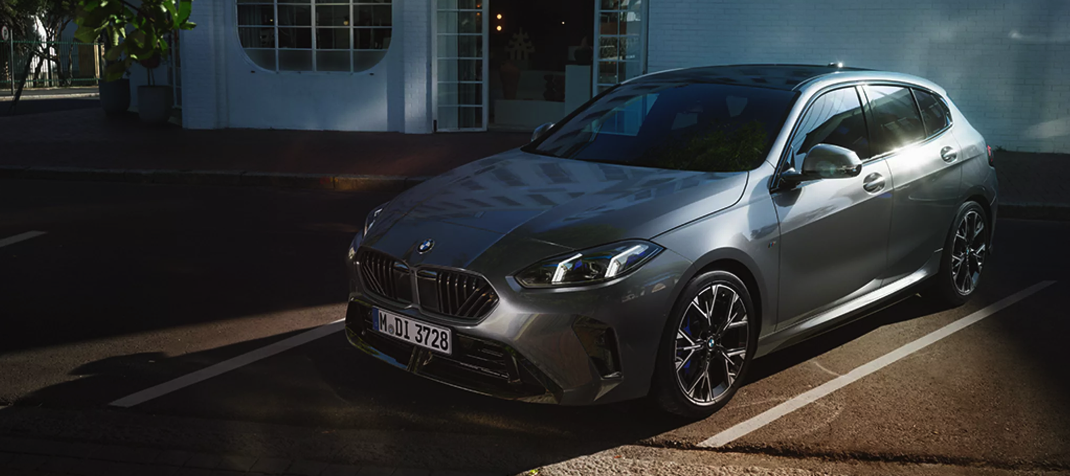 Ein silberner BMW parkt tagsüber auf der Straße in der Nähe eines modernen weißen Gebäudes.