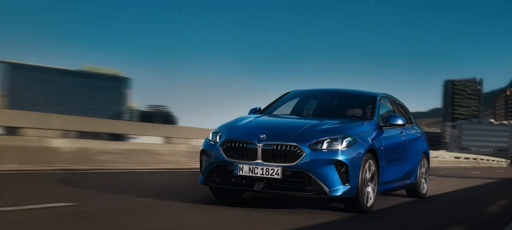 Ein schnittiger blauer BMW fährt unter dem wolkenlosen Himmel eine Stadtstraße entlang.