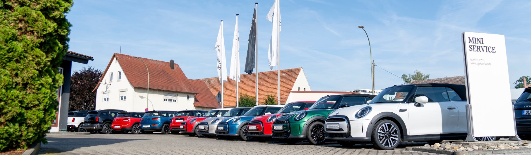 Mehrere farbenfrohe Mini Coopers mit stylischen Rädern & Reifen sind vor einem MINI Service Center geparkt.