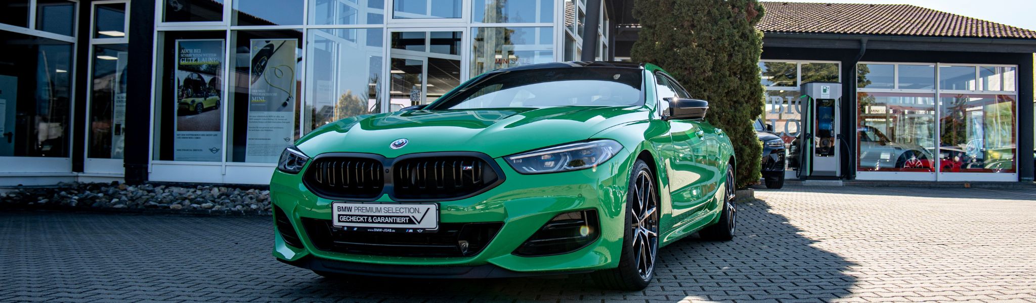 Hellgrüner BMW Jahreswagen, der an einem sonnigen Tag vor einem modernen Autohaus geparkt ist.