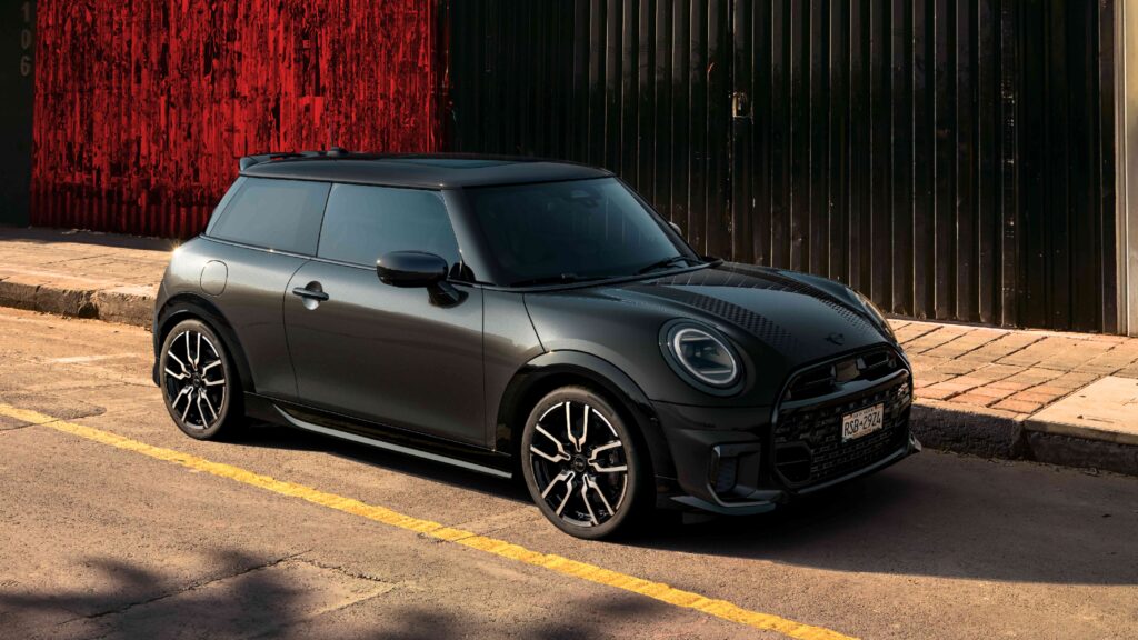 Ein schwarzer MINI Cooper parkt neben einem dunklen Industriegebäude, in der Nähe von THE i4.