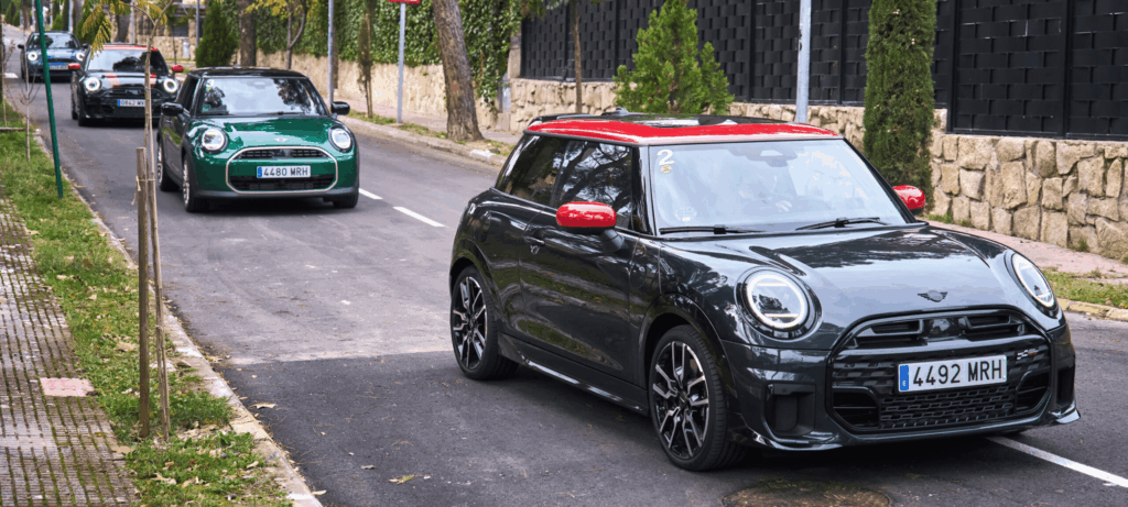 Drei Mini Coopers fahren bei lokalen Aktionen an Steinmauern und parkenden Autos vorbei.