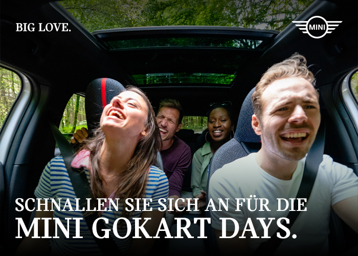 Vier Freunde lachen in einem MINI und fahren durch einen üppigen Wald.