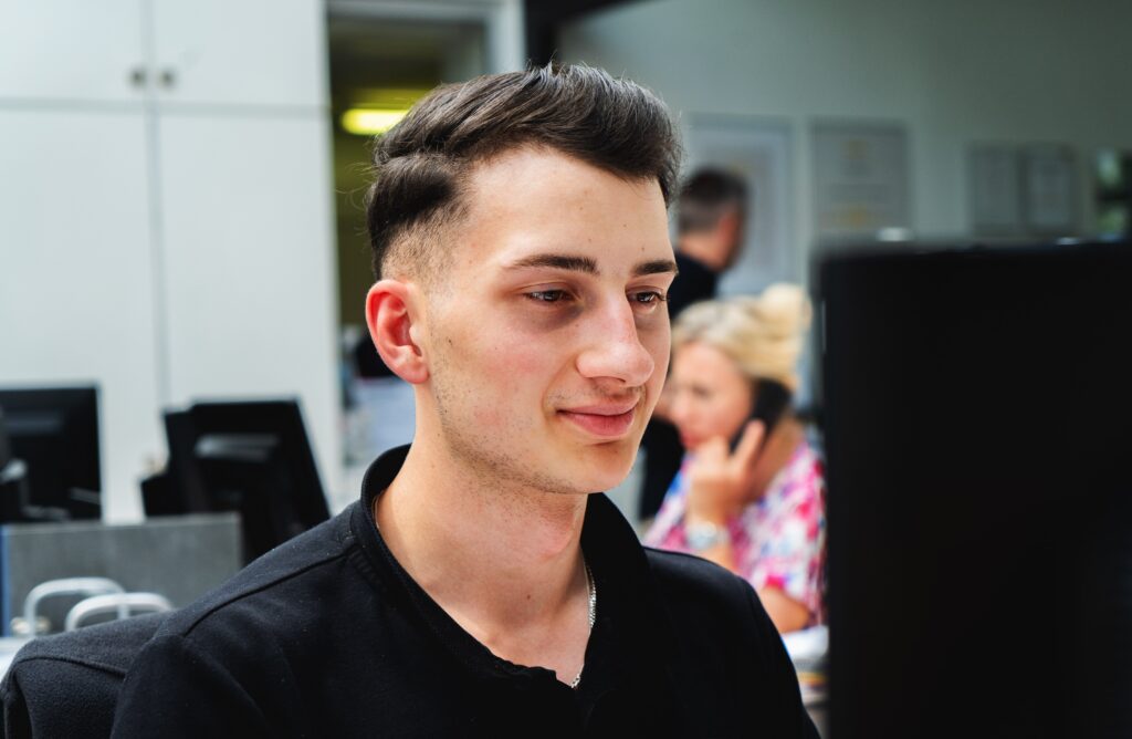 Junger Mann in schwarzem Hemd bei der Arbeit an Elektromobilitätsprojekten an einem Bürocomputer.