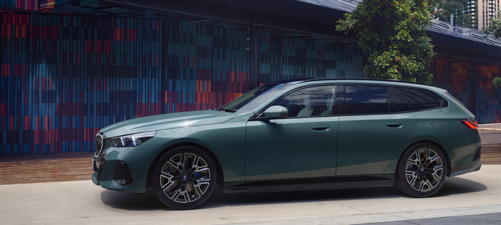 Ein grüner THE i5 Touring, der vor einem bunten, modernen Gebäude geparkt ist.
