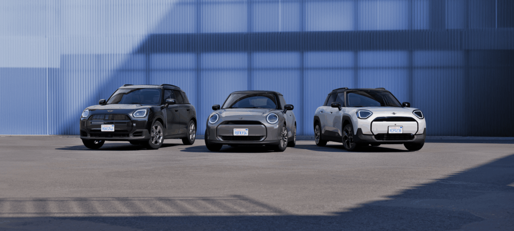 Drei Kleinwagen von der Marke MINI parken nebeneinander vor einem modernen blauen Gebäude.