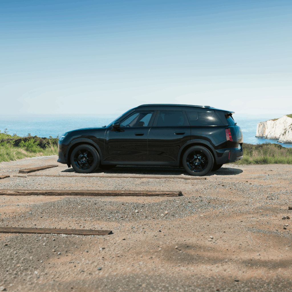 Ein schwarzer MINI Countryman steht auf einem Parkplatz vor einer Küste.