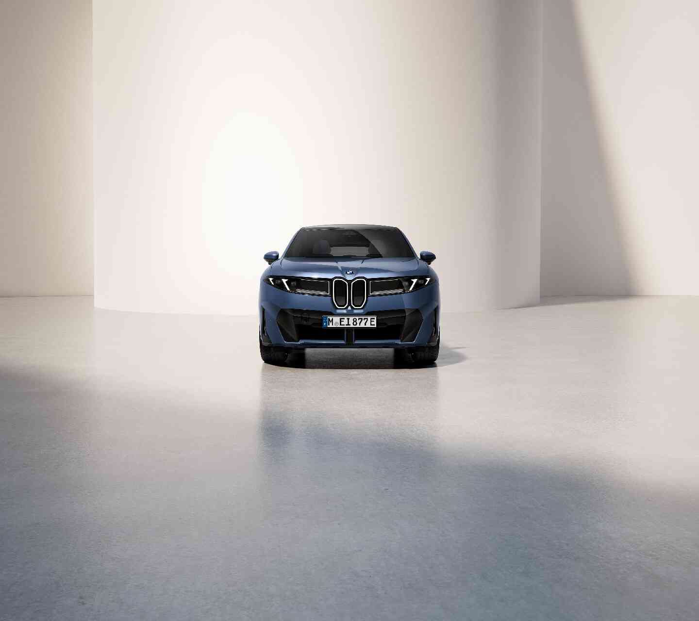 Ein blauer BMW iX 3 ist in einem Innenraum vor einer weißen, geschwungenen Wand in hellem Licht geparkt.